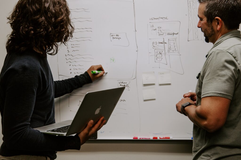 Two individuals collaborating in front of a whiteboard with a flowchart outlining a user experience strategy.