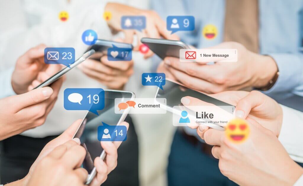 Several hands holding smartphones, surrounded by social media notifications and emojis indicating likes, comments, and messages.