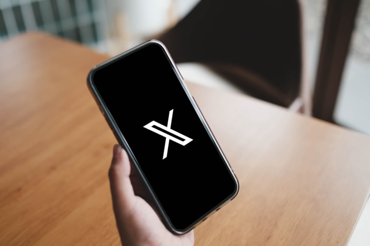 A person holding a smartphone displaying the logo of the X app on the screen.