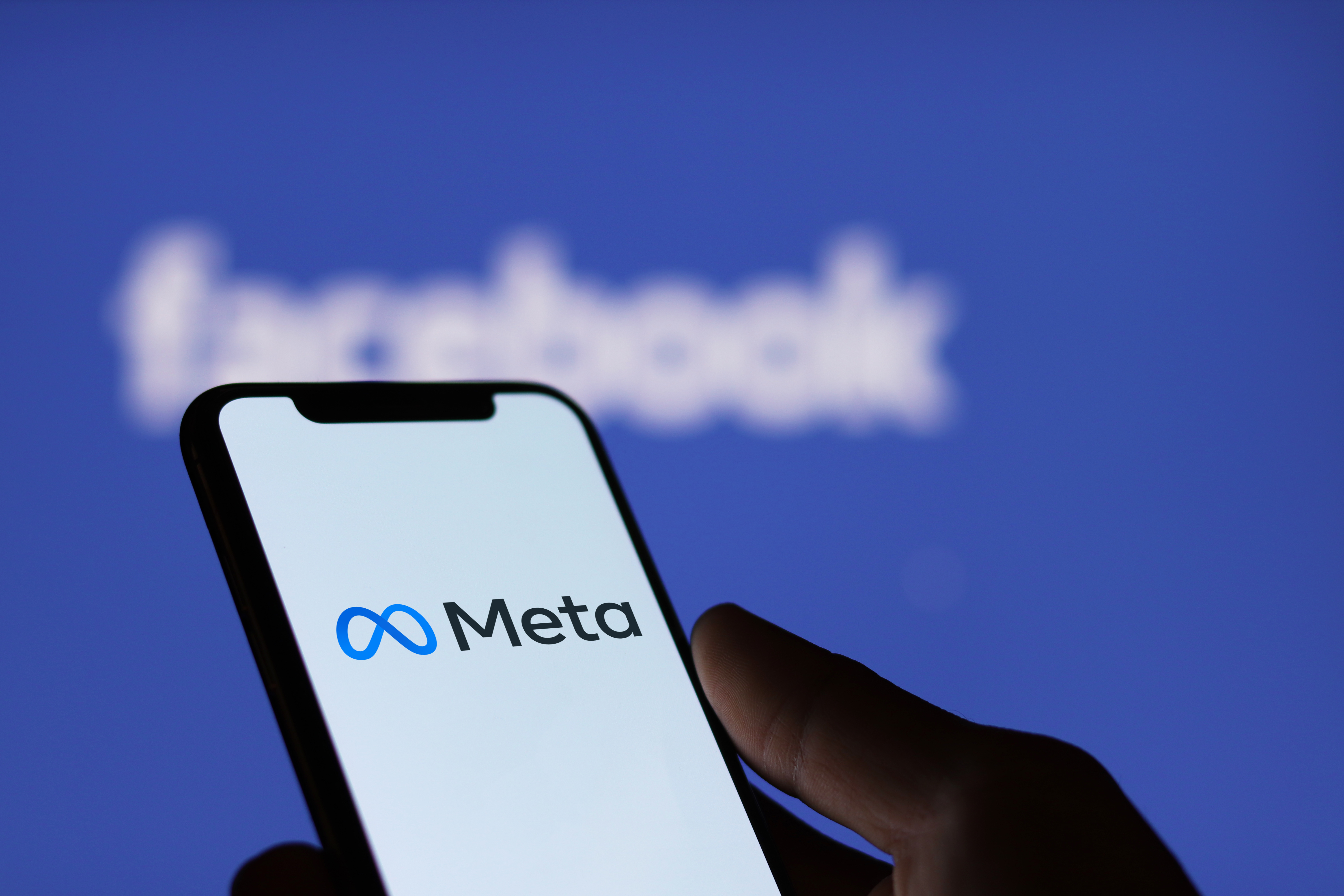 Meta logo on smartphone screen and Facebook logo background.