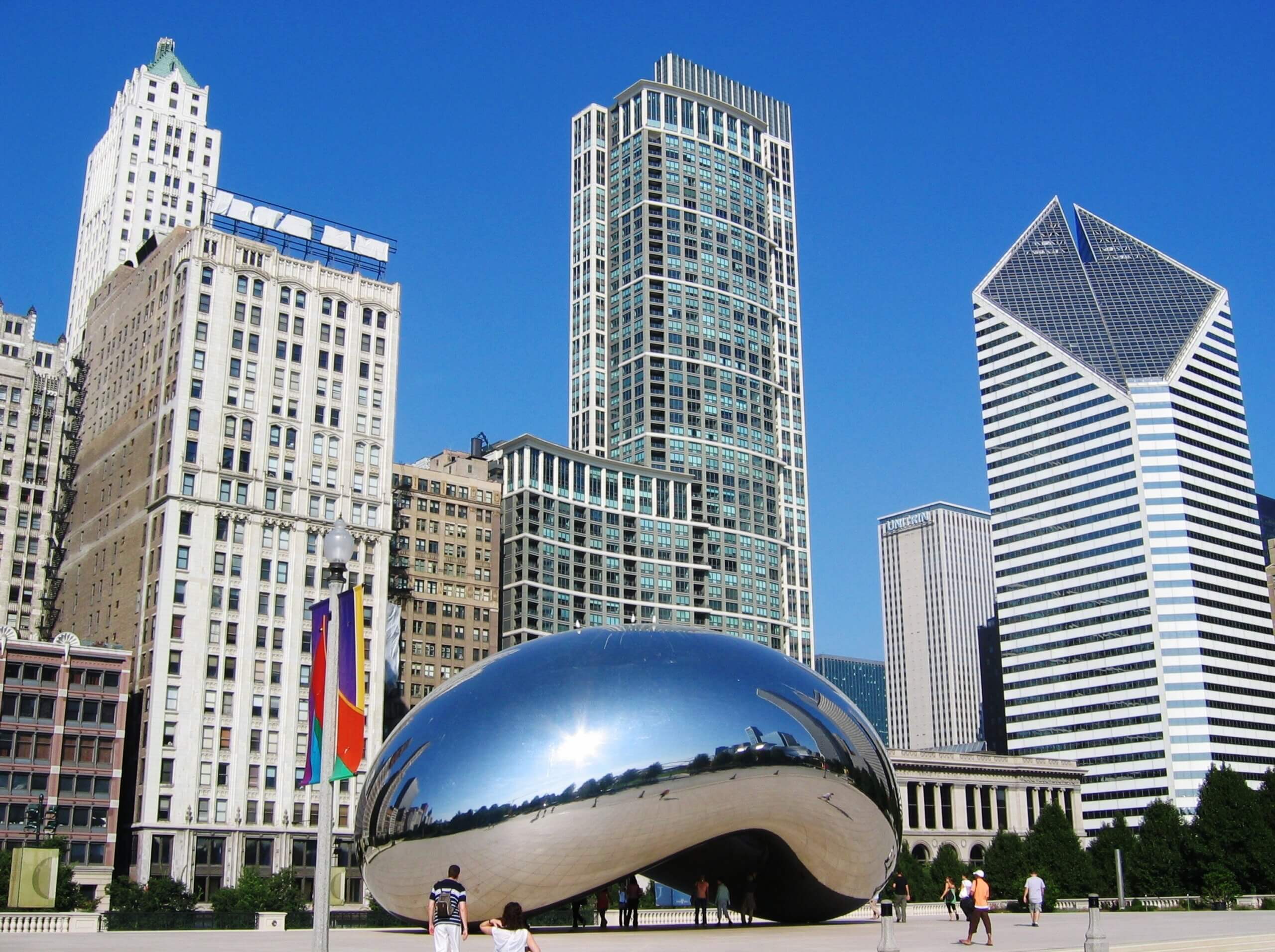 The Cloud Gate sculpture, known as “The Bean,” in Chicago’s Millennium Park reflecting the city skyline, with several tall buildings and a bright blue sky in the background.