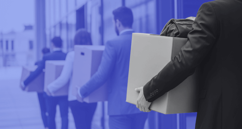A line of business professionals walking while carrying boxes of personal belongings, suggesting layoffs or employees leaving an office building, with a blue-toned background.