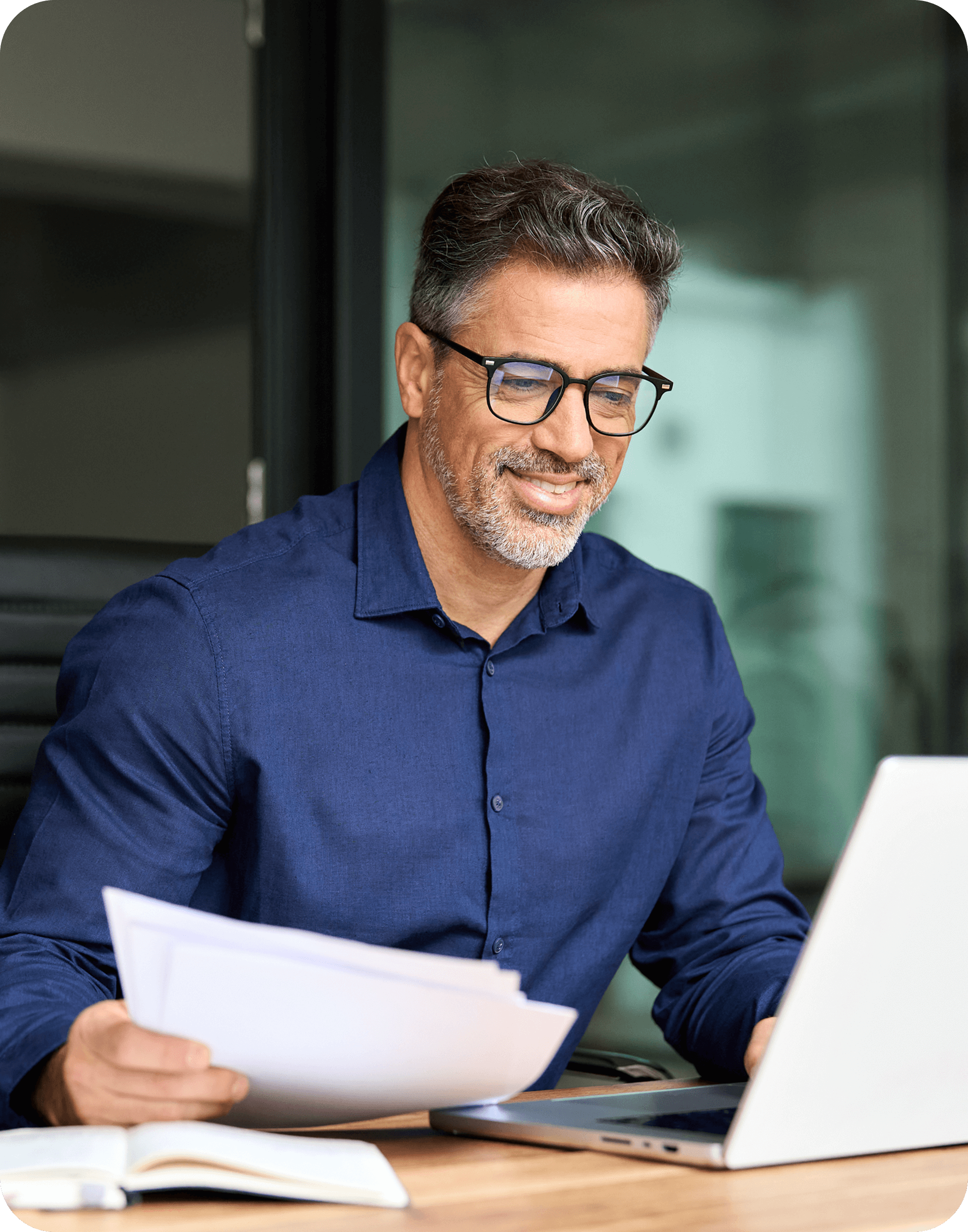 Smiling man working at laptop with documents.