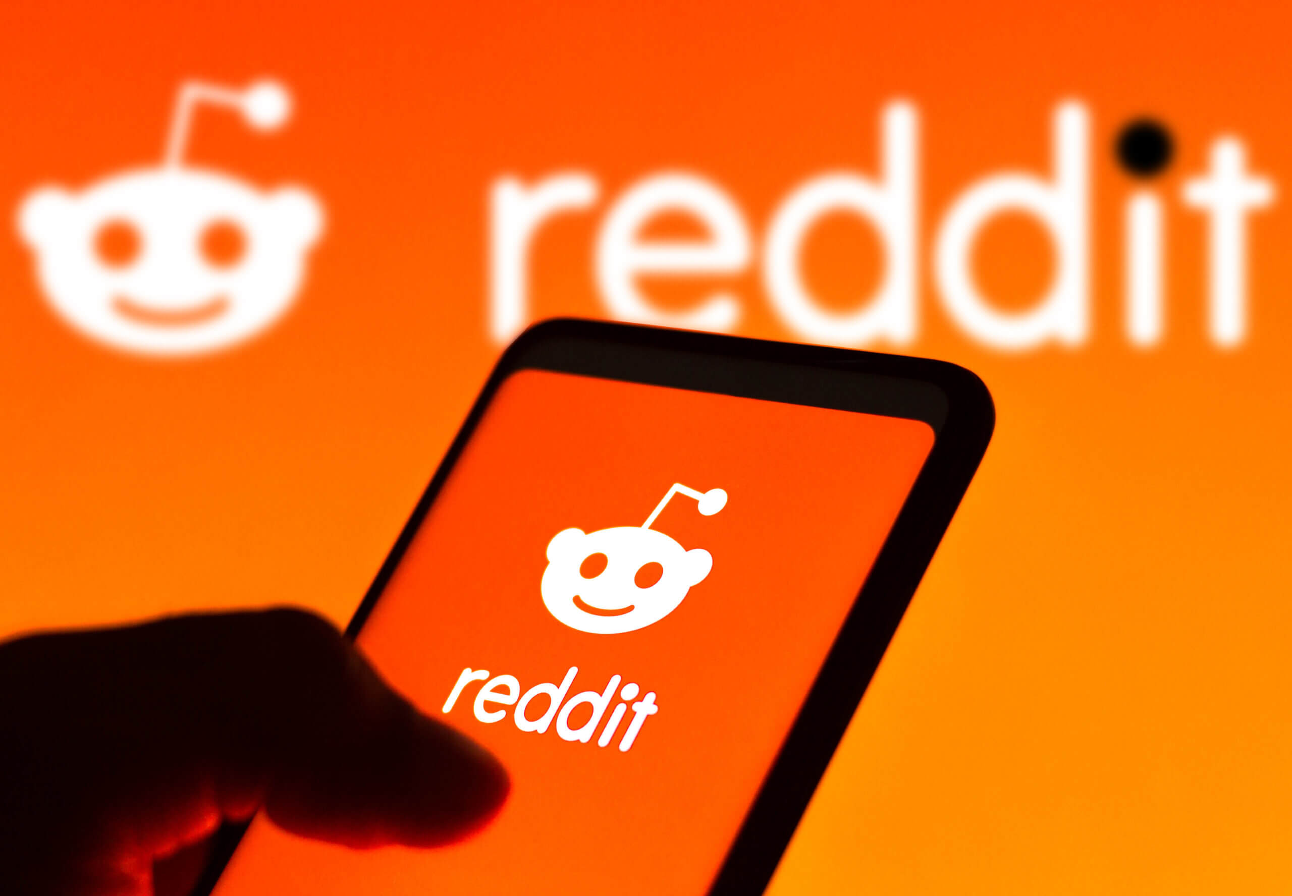 In this photo illustration the Reddit logo seen displayed on a smartphone and on the background