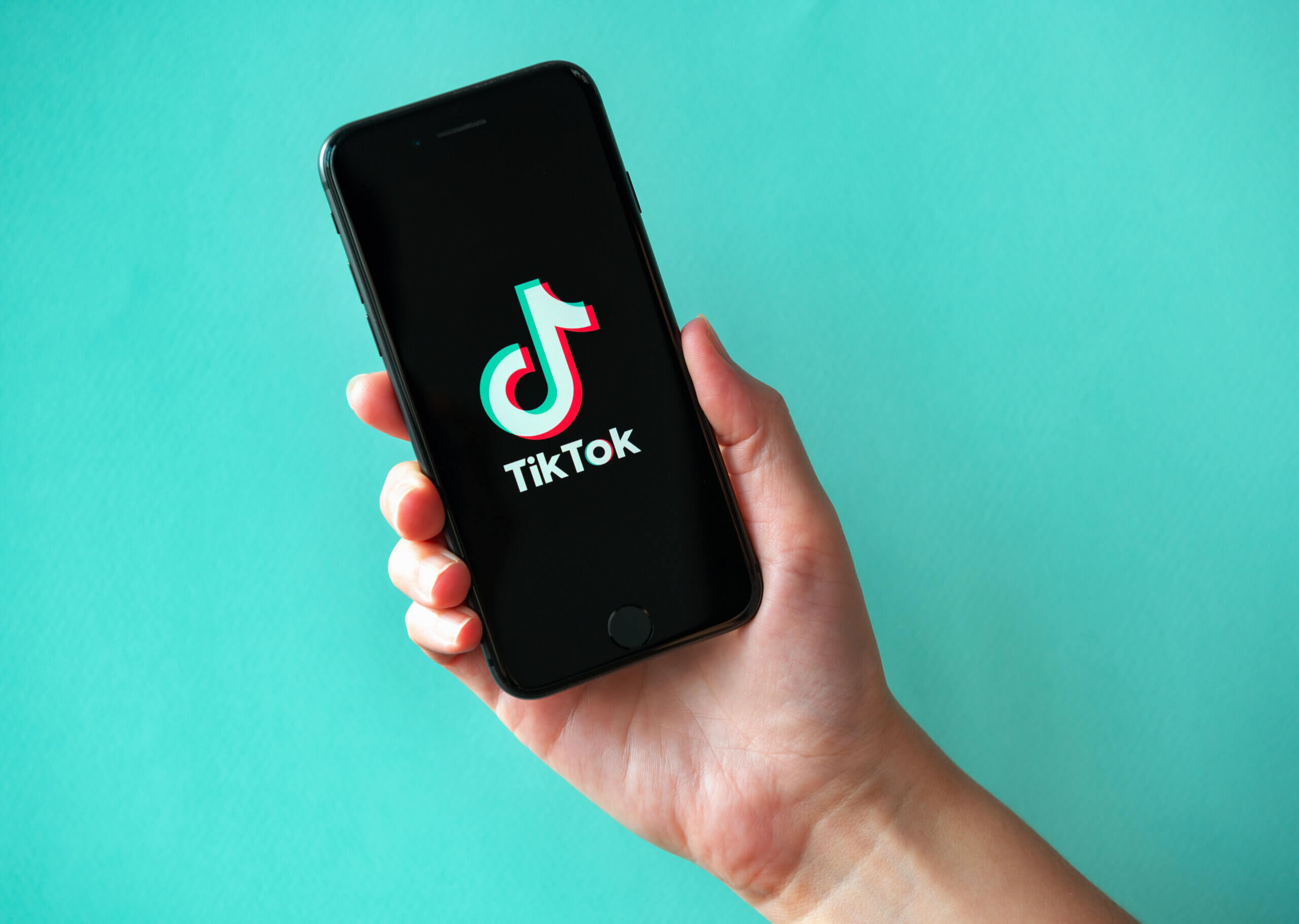 Studio shot of hand holding Apple iPhone 8 with TikTok logotype on a screen. Isolated on a vibrant cyan paper background.