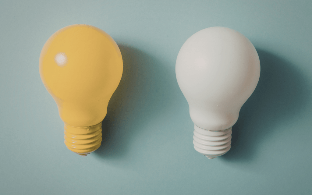Two light bulbs on a light blue background. One on the left is yellow, while the one on the right is white.