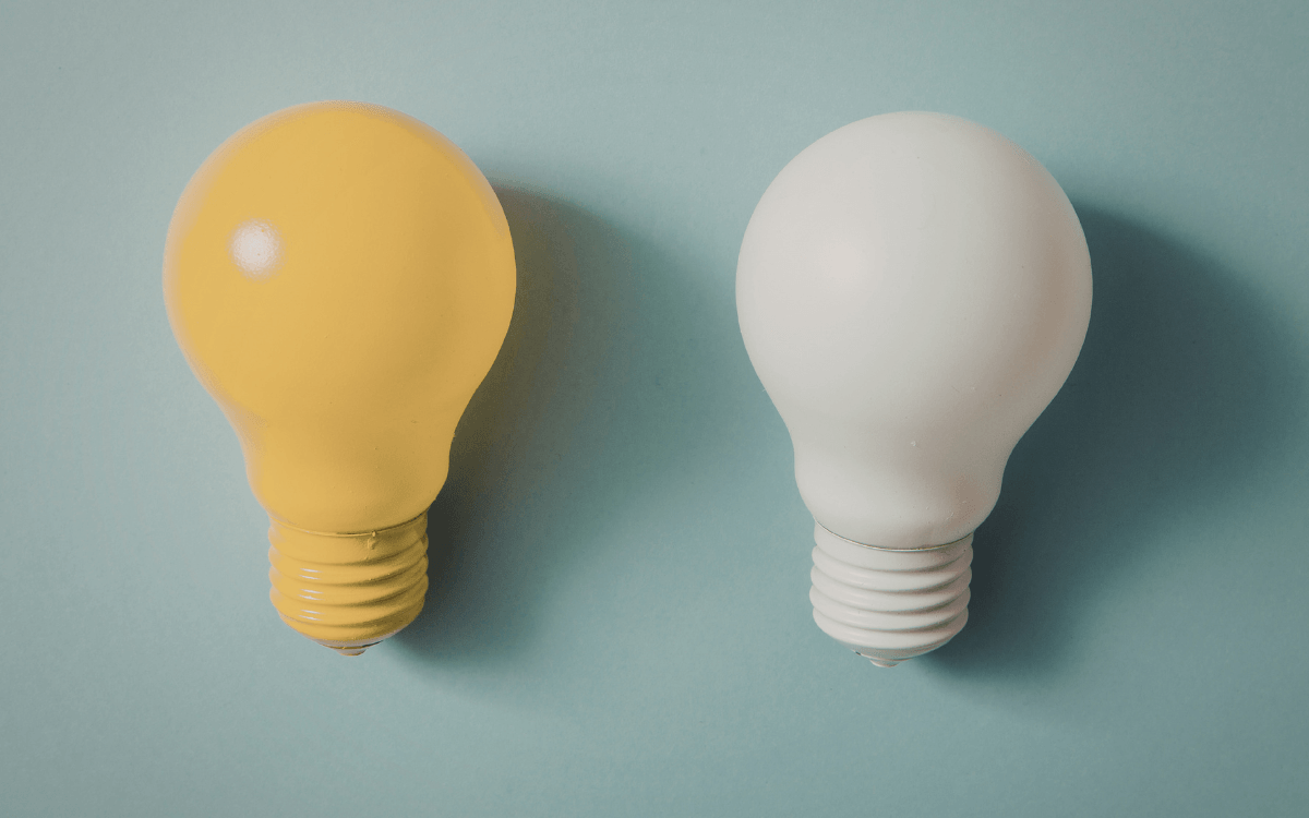 Two light bulbs on a light blue background. One on the left is yellow, while the one on the right is white.